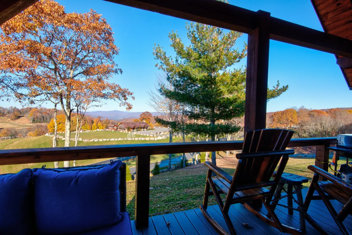 A tranquil wooden deck set with classic rocking chairs, framed by autumn foliage and distant mountains. The arrangement suggests quiet mornings, cozy afternoons, and peaceful evenings with opportunities for stargazing and enjoying the changing mountain landscape.