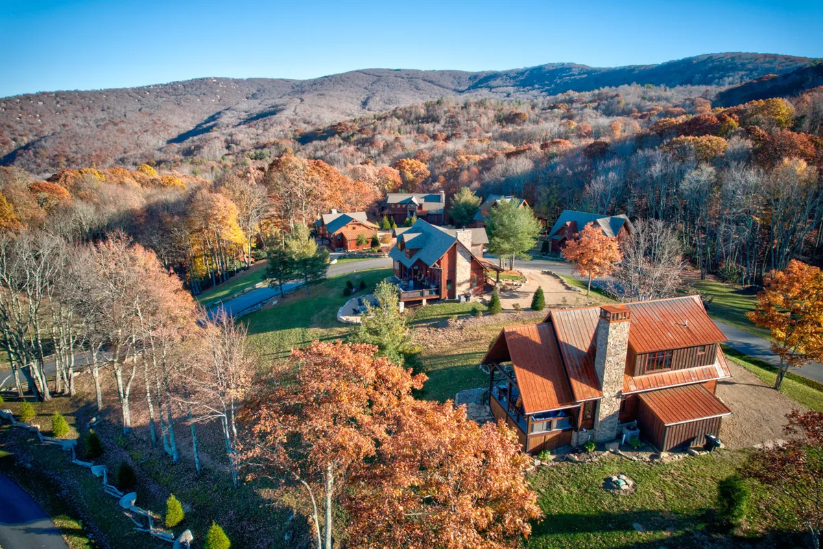 A wide view of the property shows a mountain backdrop with colorful autumn trees, spacious lawns, and rustic resort-style architecture. Groups gather for hiking, family barbecues, or simply to soak in the tranquil environment. The atmosphere is both inviting and serene, with hints of stargazing and fall foliage walks.