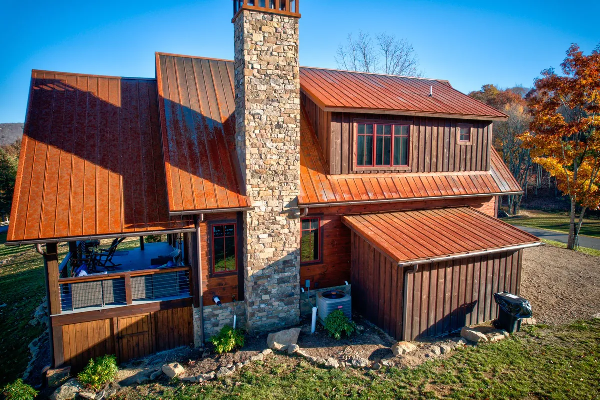The home’s welcoming exterior is shown with a stone chimney, wooden siding, and a landscaped yard, featuring ample space for outdoor activities like barbecues or gatherings around the fire pit. The porch offers views of the mountains and seasonal gardens.