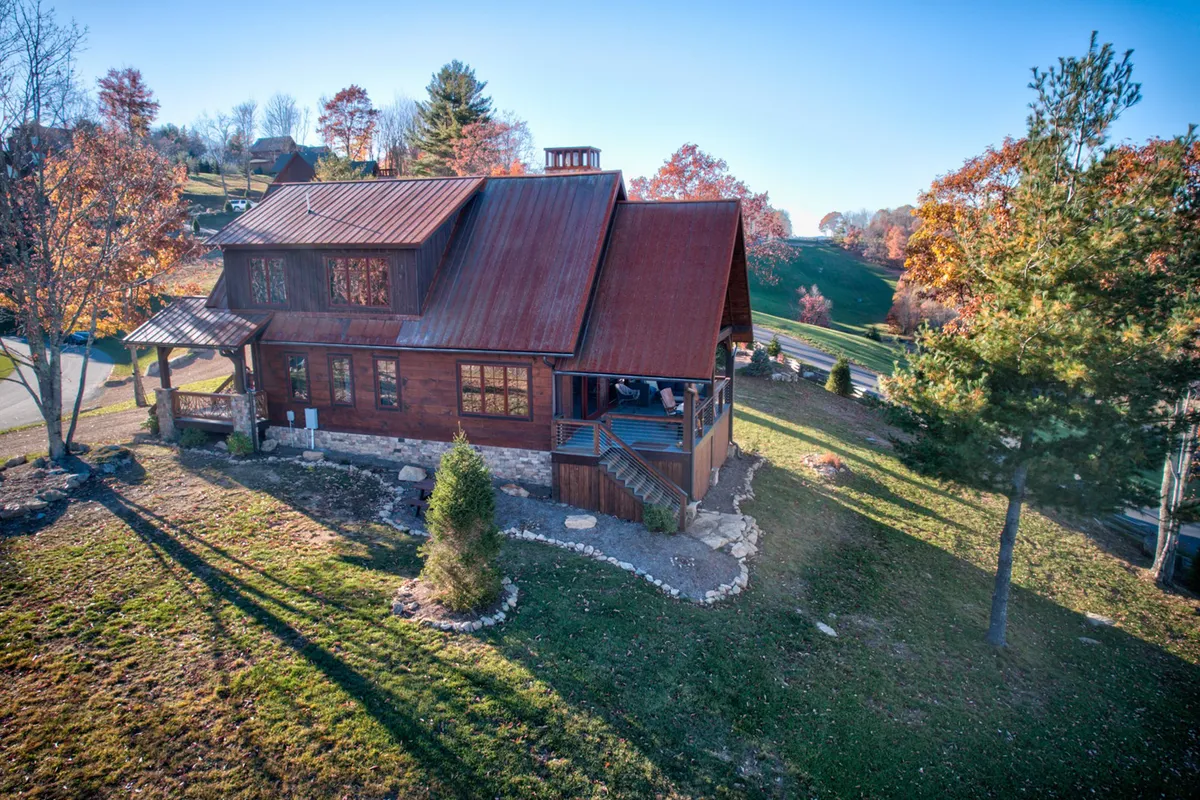A cozy, inviting exterior shot of the home featuring a rustic wooden façade, a bold red metal roof, and beautifully landscaped gardens surrounded by lush trees. The porch promises an idyllic spot for morning coffee or evening gatherings, perfectly blending luxury with the mountain environment.