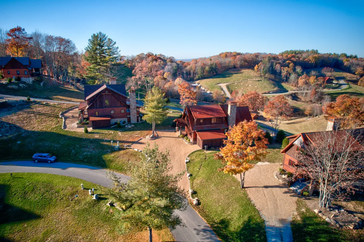 A cluster of rustic cabins nestled among colorful autumn trees, with a winding road leading through the landscape. The setting conveys a sense of peaceful seclusion and connection to nature, as well as opportunities for hiking and exploring.