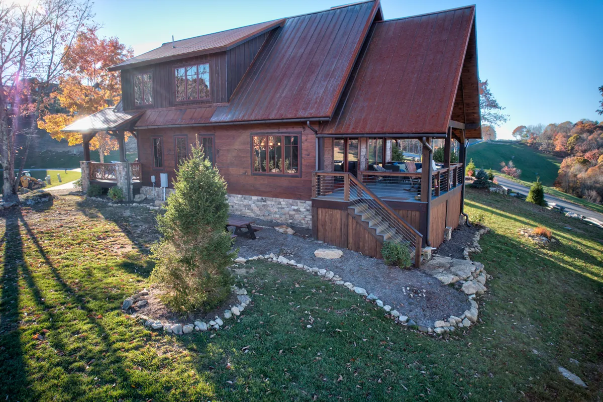 A wide-angle exterior view presenting a rustic home with a metal roof, landscaped garden, and a welcoming outdoor seating area. The setting is peaceful, surrounded by greenery, and invites guests to step outside for gatherings or to explore the natural environment.
