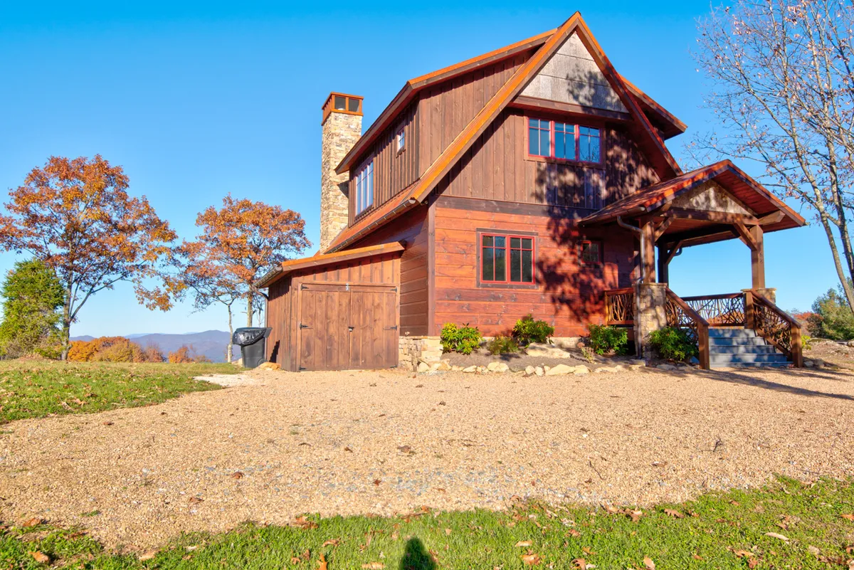 A warm, inviting exterior view of the house showcasing its wooden façade, stone chimney, and a spacious porch. The porch is perfect for gathering, relaxing, and taking in the surrounding natural beauty after a day of adventure.