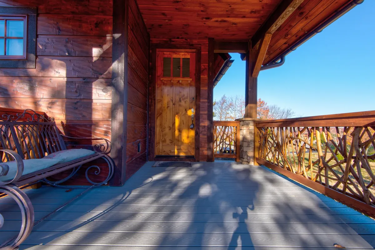 A cozy exterior porch scene featuring a wooden door, ornate bench, and decorative railing. Guests are shown relaxing on the bench and socializing, with an inviting ambiance ideal for enjoying sunset views or morning tea.